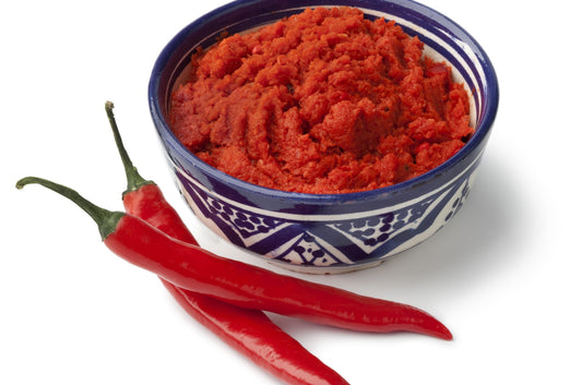 Bowl of red chili paste with whole red chilies on a white background